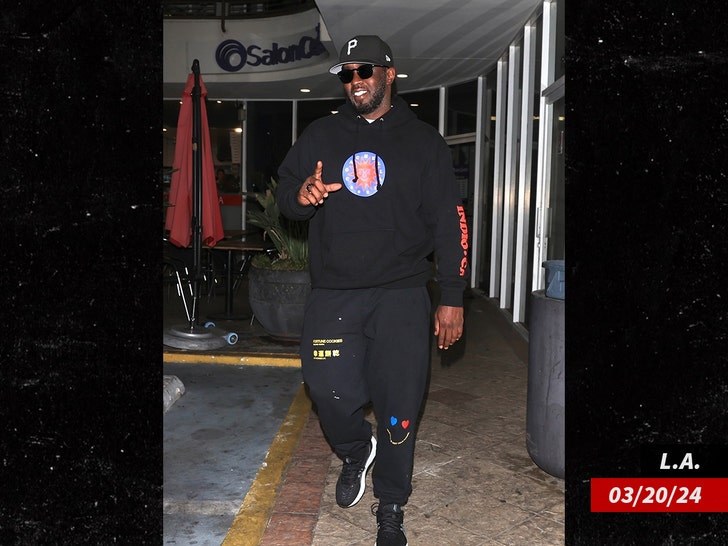 Diddy walking through a shopping mall wearing black sweatpants, a black hoodie and a black hat.